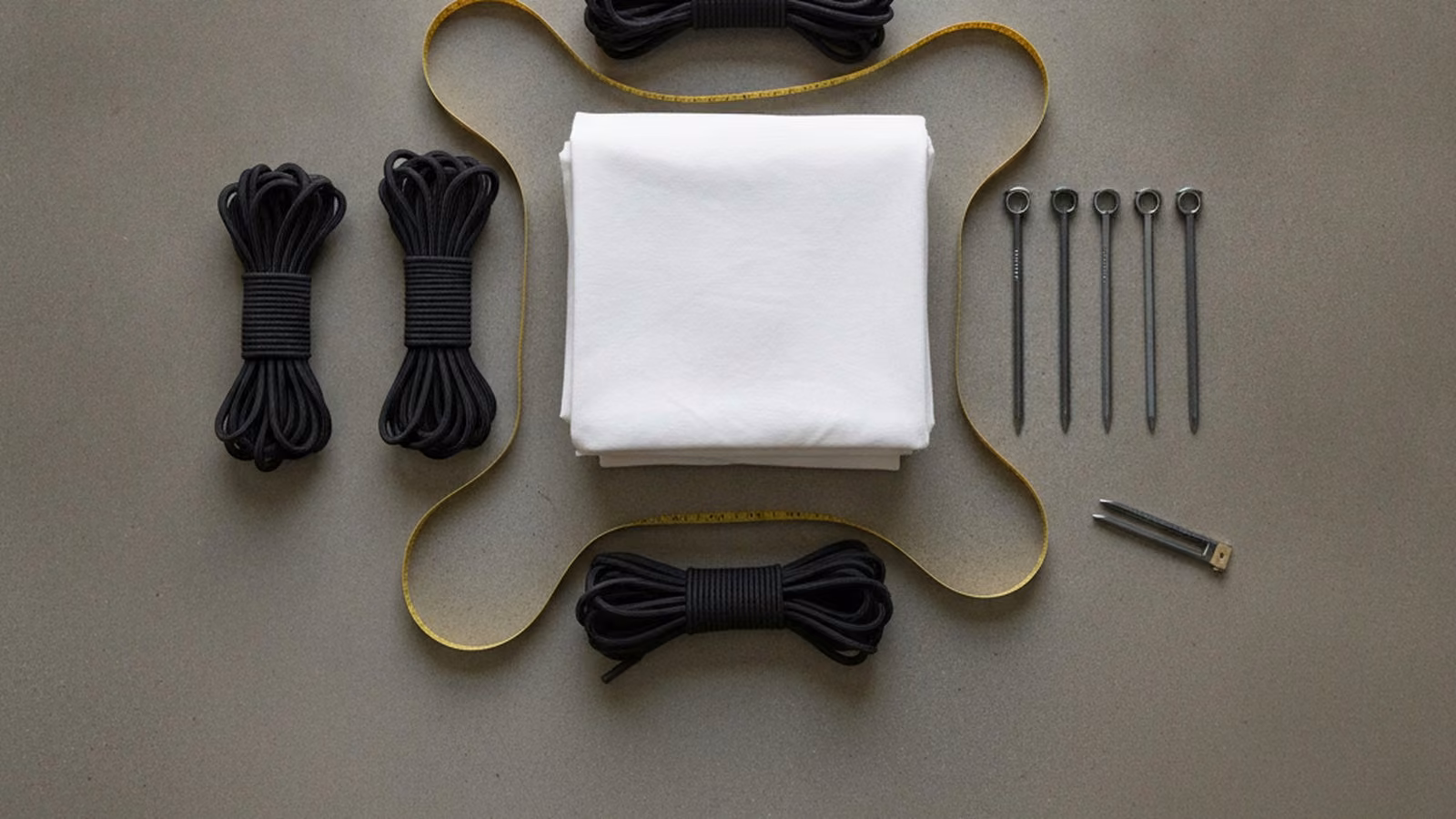 Folded tent canvas, guy ropes, steel stakes and a measuring tape laid out