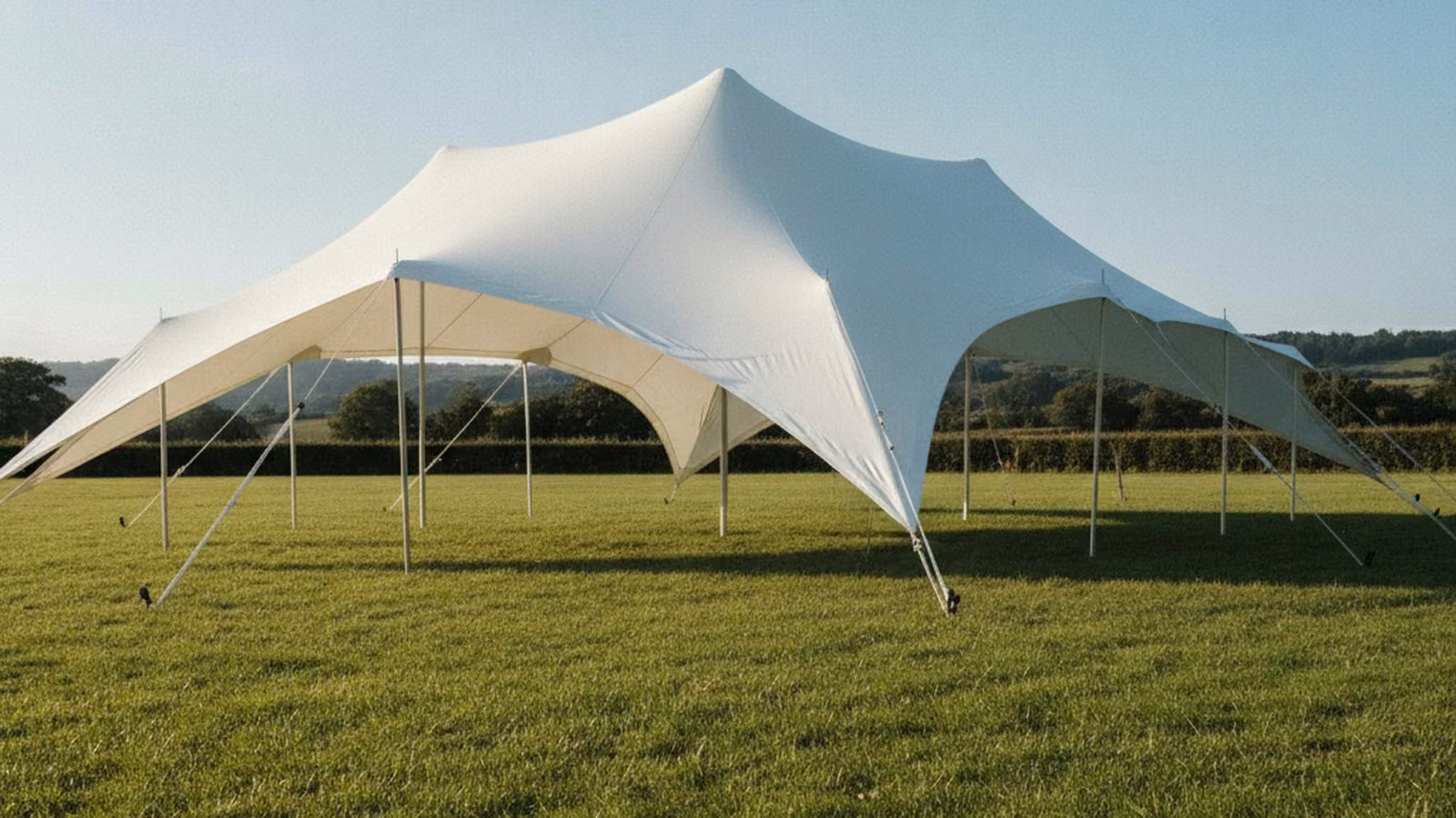 A white stretch tent with curved peaks pitched on grass